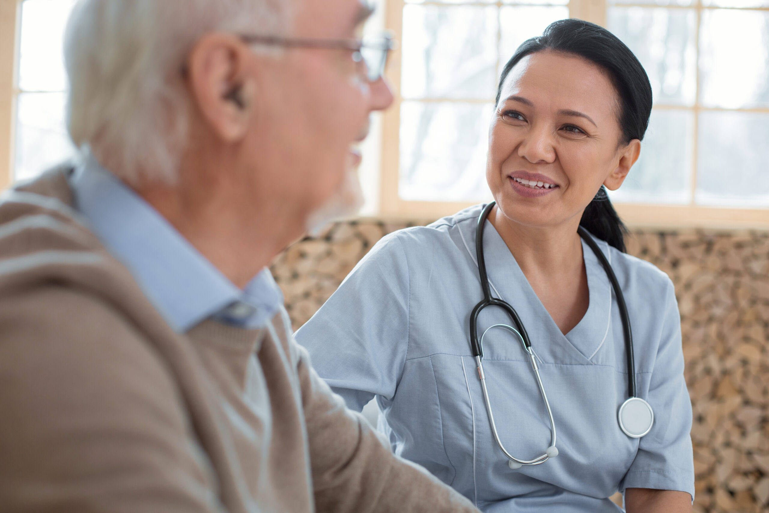 Appealing happy doctor wearing uniform while gazing at senior man and smiling